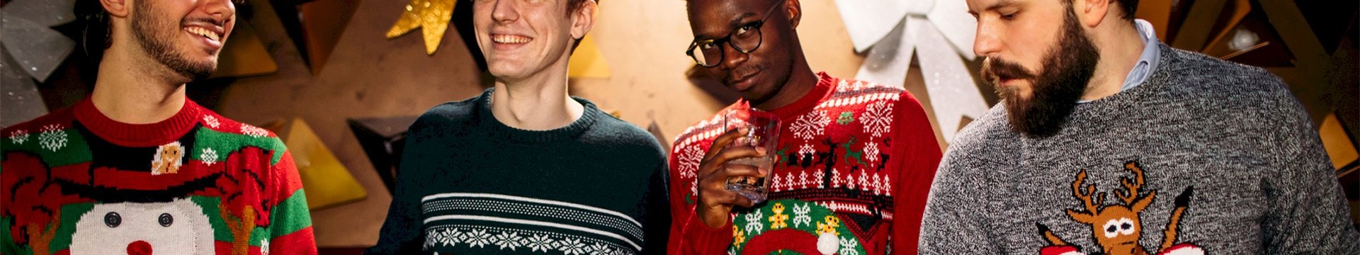 Four men in christmas jumpers enjoying a beer.