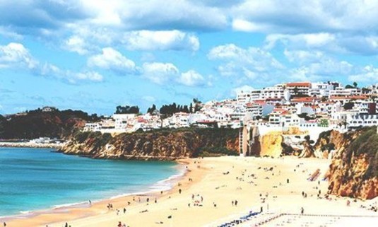 Looking up at Albufeira's buildings on a cliff by the water. Discover Albufeira Stag Party ideas below: