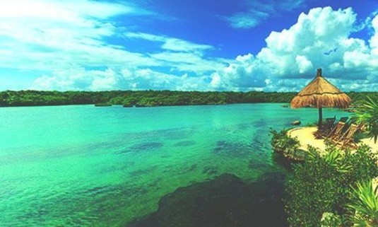 Beautiful blue sky over the emerald waters of the Caribbean Sea with beach chairs on the sand. Explore Cancun Stag Party ideas below: